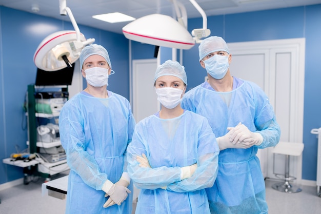 Team of three contemporary surgeons in masks, gloves and protective uniform