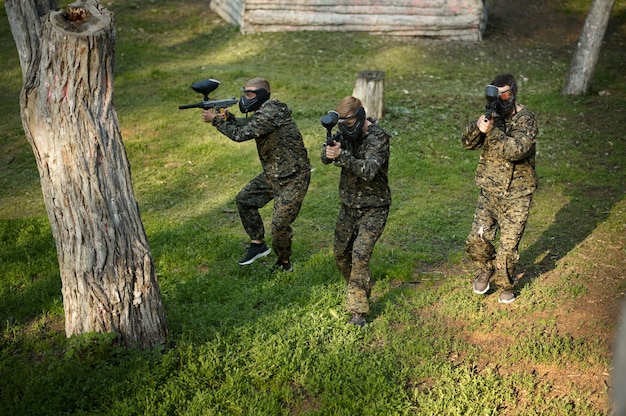 Foto squadra in uniforme e maschere che giocano a paintball, battaglia nel parco giochi nella foresta. sport estremo con armi pneumatiche e proiettili o pennarelli di vernice, gioco militare all'aperto, tattiche di combattimento