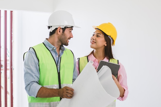 Team van glimlach jonge blanke, Aziatische man en vrouw aannemer, partner legt uit en inspecteert de gereconstrueerde constructie en gerenoveerd om defect van appartement, huis, huis op de bouwplaats, werkplek te controleren.