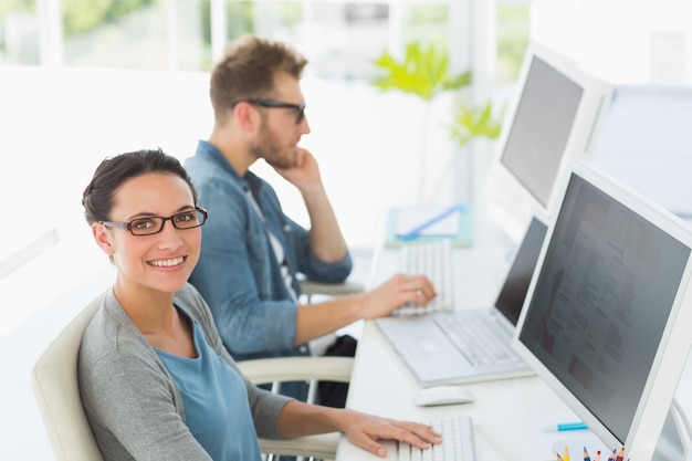 Team van jonge ontwerpers die bij bureau met vrouw werken die bij camera glimlachen