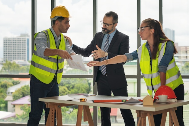 Team van multi-etnische architecten bezig met bouwplannen in de vergaderruimte. Ingenieurs bespreken op project in kantoor. Rijpe zakenman en vrouw die zich rond lijst bevinden die aan blauwdruk werken.