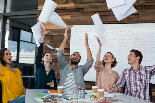 Team van opgewonden grafische ontwerpers gooien document in de lucht tijdens de vergadering