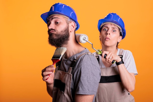 Team van schilders met penseel en roller in de studio, bezig met schilderen met gereedschap. Experts in bouwvakkers die overalls dragen en poseren met borstels, bezig met renovatieprojecten.