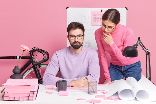 Team van vrouwelijke en mannelijke architecten werken aan blauwdruk werken samen aan nieuwbouwproject poseren op desktop met papieren omringd met stickers