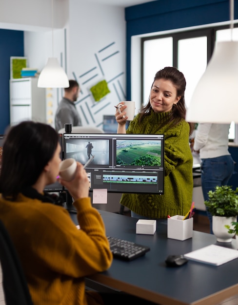 Team di videografi che parlano del progetto mentre bevono caffè lavorando nell'app di editing video al pc seduti in una società multimediale digitale