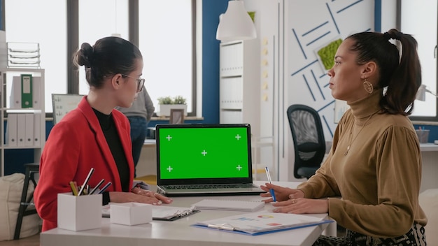 Team of women working with green screen on laptop in business office. Coworkers using mock up template with isolated chroma key background on display. Chroma-key copy space on screen