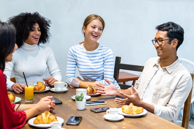 バーのテーブルで朝食クロワッサンコーヒーとカプチーノを持っている若いミレニアル世代のリラックスしたグループの瞬間にチームワーク