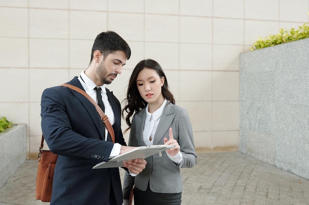 Team of young business people discussing details in sales report when standing outdoors