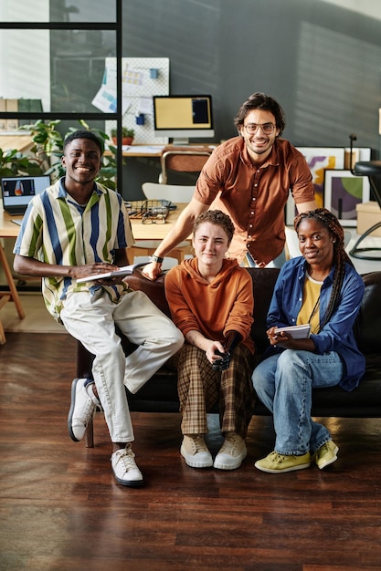 Team of young cheerful managers sitting on couch in office