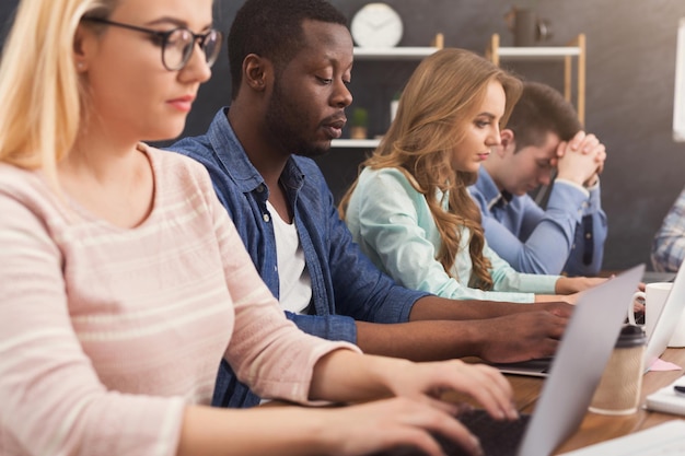 Team di giovani programmatori che lavorano in società di sviluppo software, digitando su laptop, testando nuovi giochi o app, copia spazio