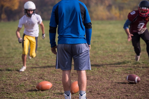 Teamcoach gooit de bal in de groep jonge Amerikaanse voetbalspelers in actie tijdens de training op het veld