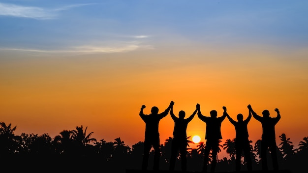 Teams die bereid zijn om succes te delen, staan samen in handen om naar de zonsondergang te kijken.