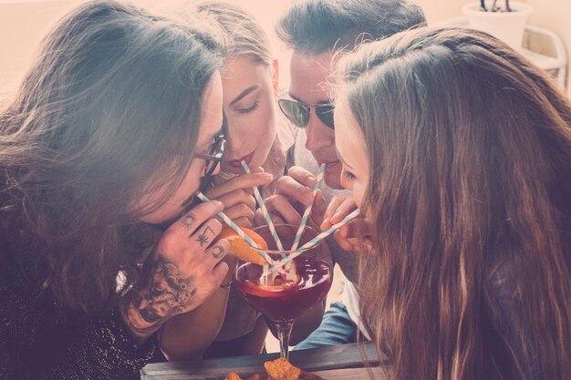 Teamvrienden blanke jonge mensen die plezier hebben tijdens het vieren en allemaal samen uit hetzelfde cocktailglas drinken