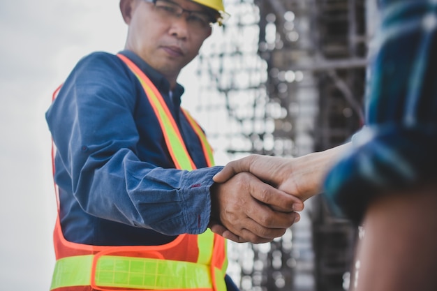 Teamwork Engineer schudt de hand op de bouwachtergrond van de site