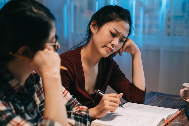 teamwork thinking brainstorming concept. two young college girls classmates working together at late night at home. frowning asian women friends consider about mathematics problem prepare for test