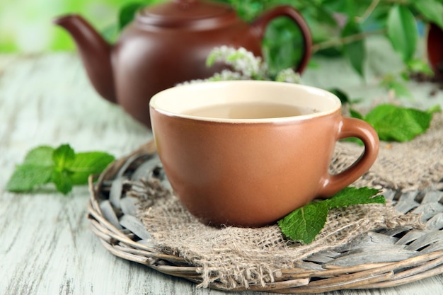 Teapot and cup of herbal tea with fresh mint flowers on wooden table