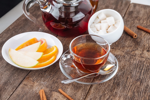 Чайник и чашка с нарезанными фруктами и сахаром на деревянном столе
