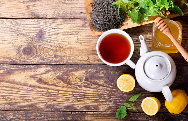 Teapot and cup of tea with mint and lemon on wooden table, top view