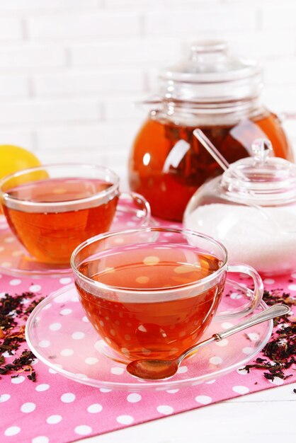 Teapot and cups of tea on table on brick wall background