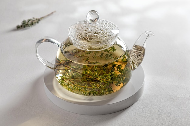 Teapot of hot herbal tea with thyme on white tray and white background in the rays of the sun