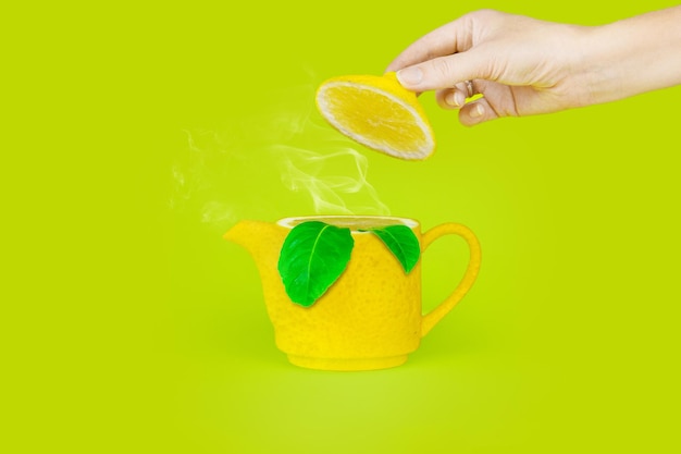 蒸気とレモンの形のティーポット、緑の背景にレモンの葉。イングリッシュティータイムのコンセプト。お茶の醸造と飲用。