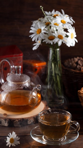 A teapot and a mug of tea on a wooden table and a bouquet of daisies