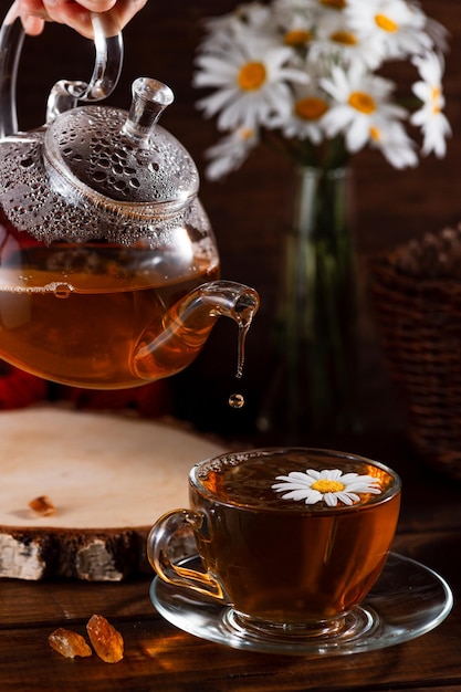 ティーポットと木製のテーブルの上のお茶のマグカップとヒナギクの花束