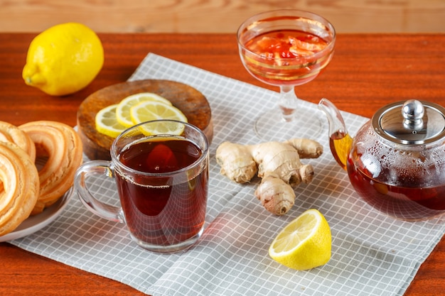 Чайник крепкого чая и чашка на столе рядом с имбирем и лимоном, пончики со сливками на салфетке.