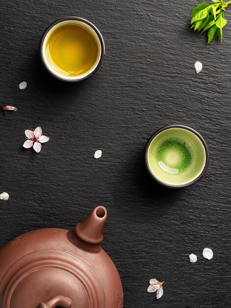 Teapot and small cups with green tea are located on a black stone table