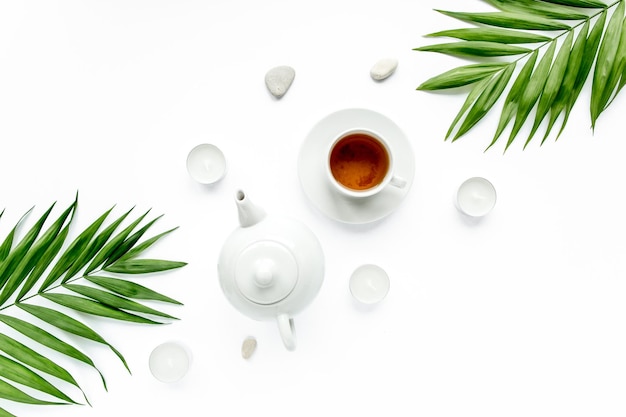 Teapot tea mug and palm leaf branches flat lay top view