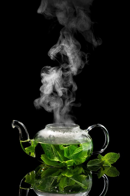 Photo teapot with brewed mint tea on a black with rising steam above it