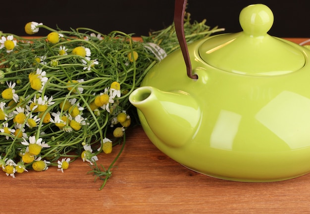 Teapot with chamomile tea on wooden table close-up
