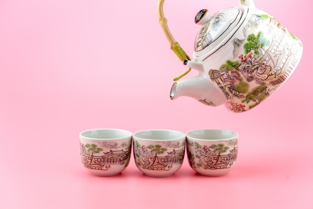 Чайник с чашками на розовом фоне.