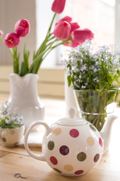 Teapot with dots and vases with beautiful spring forgetmenots and tulips flowers on a wooden table