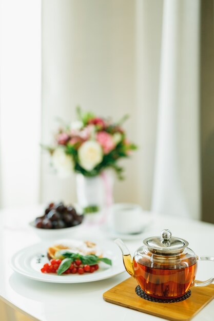 A teapot with tea on a dostochka on a table with plates and a bouquet of flowers on a blurred