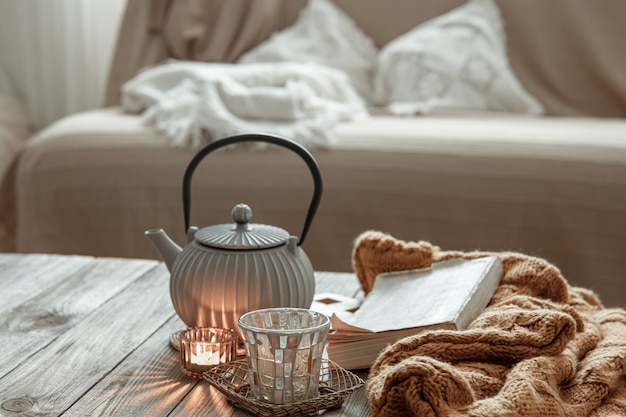 Teapot with tea, knitted item and candles on the table in the interior of the room.