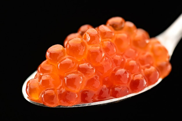 Teaspoon filled with red caviar on black