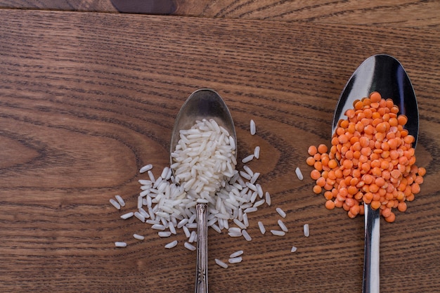 Teaspoon of rice and tablespoon of orange lentils. Brown wooden background.