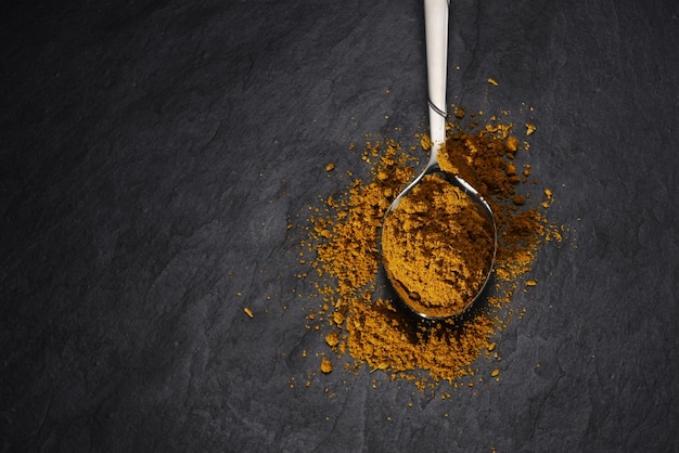 Teaspoon with curry powder spice on black slate background