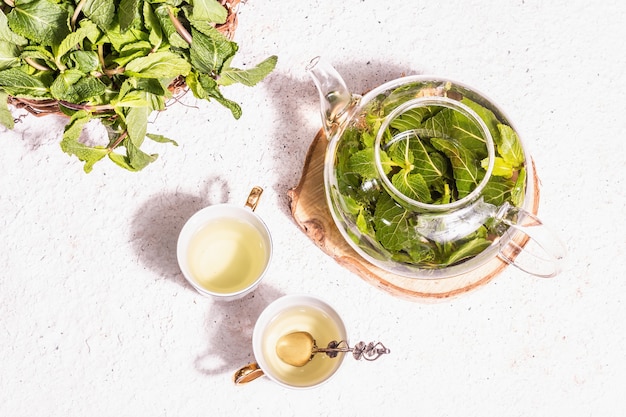 Concetto di ora del tè. tè alla menta aromatico, tazze in ceramica su supporti. luce dura moderna, ombra scura. sfondo in gesso, vista dall'alto