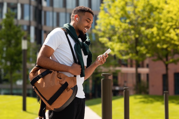 Tech gadgets for entertainment happy african american guy walking and using smartphone outdoors in