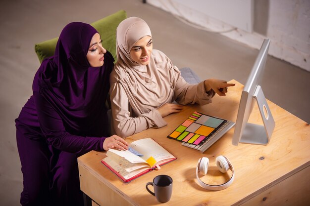 Tech Happy and young two muslim women at home during lesson sitting in armchairs