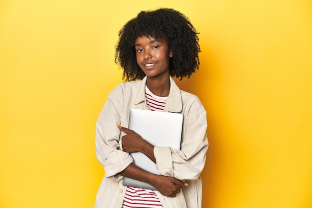 Tech-savvy Afro-Amerikaanse tienermeisje met laptop op gele studio achtergrond