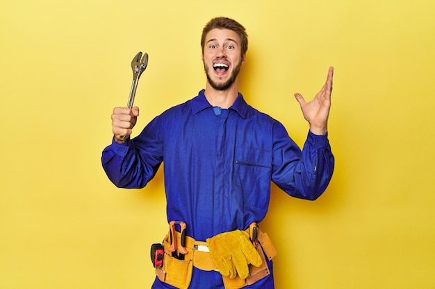Photo technician in blue jumpsuit with tools on yellow receiving a pleasant surprise excited