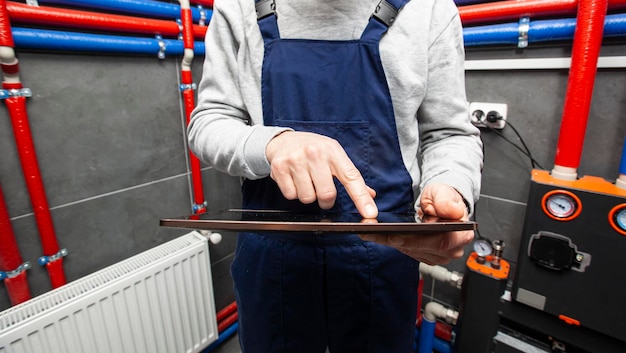 Photo the technician checking the heating system in the boiler room with tablet in hand