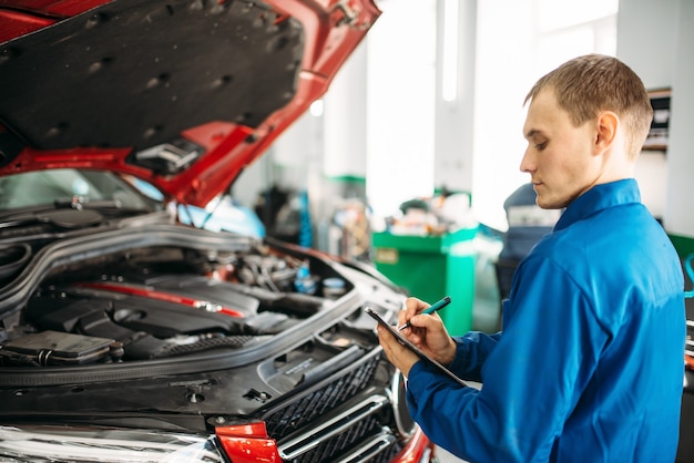 Technician fills check list, car with opened hood