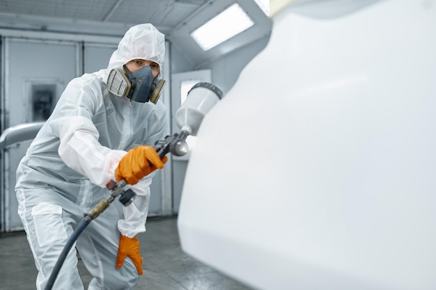 Technician hand in safety clothing spraying paint and varnish on car body part