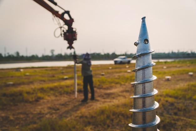 Photo technician installing ground screw for mounting structure of solar panel at solar farm