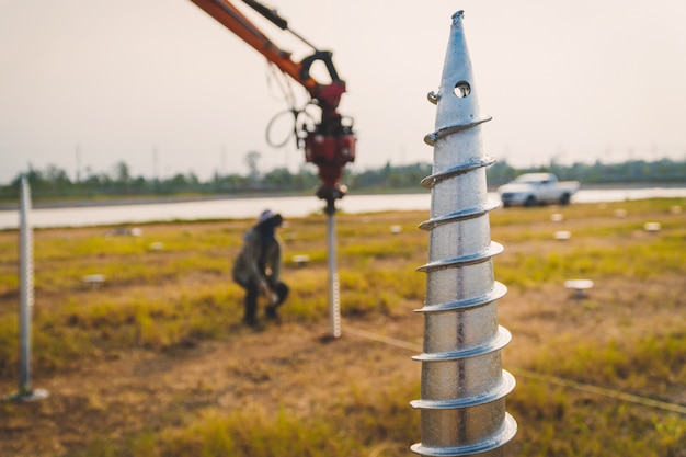 Technician installing ground screw for mounting structure of solar panel at solar farm