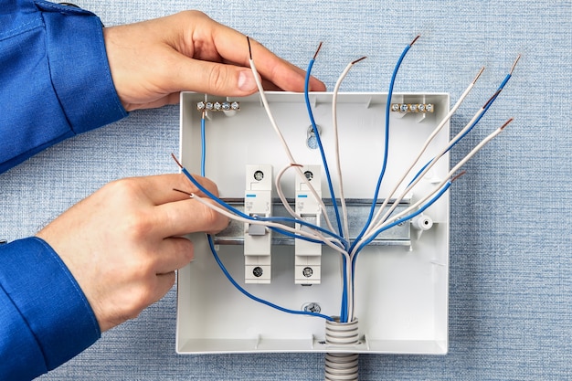 Technician installing a new switchboard with automatic fuses for household electrical wiring.